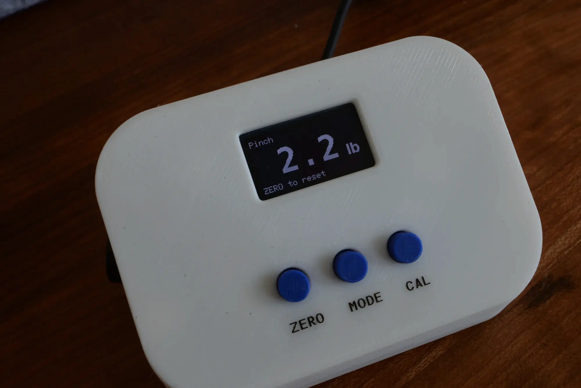 Splayometer device on a wood surface, OLED display showing a Pinch reading of 2.2 lb
