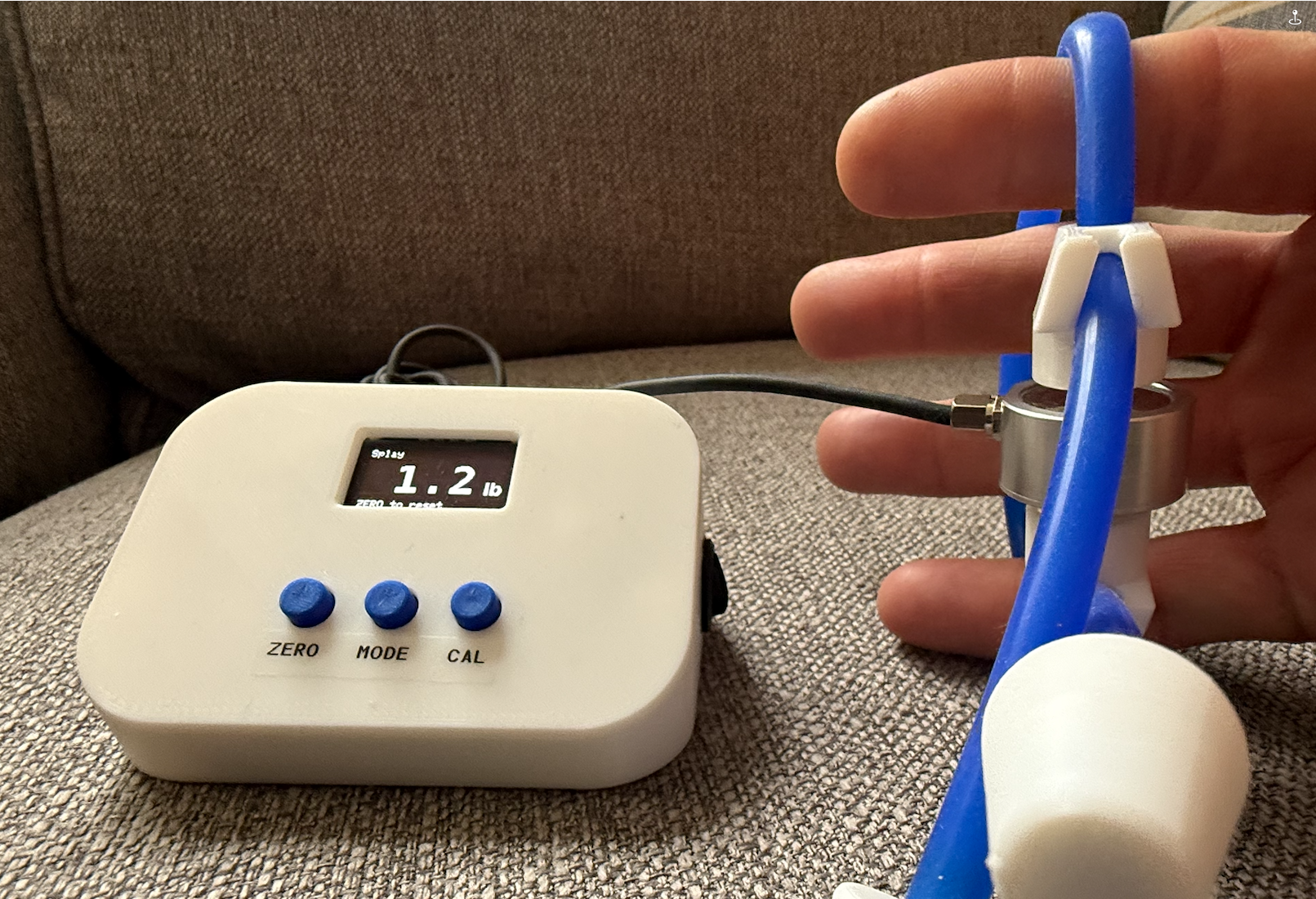 Hand inside the Splayometer hand loop attachment with the device displaying a real-time force reading